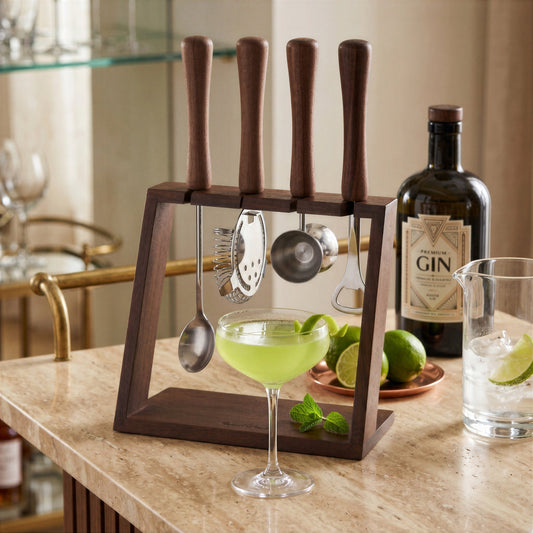 Final Touch acacia wood and stainless steel 5-piece bar tool set with stand, displayed on a marble countertop next to a green cocktail in a coupe glass, fresh limes, and a bottle of gin.