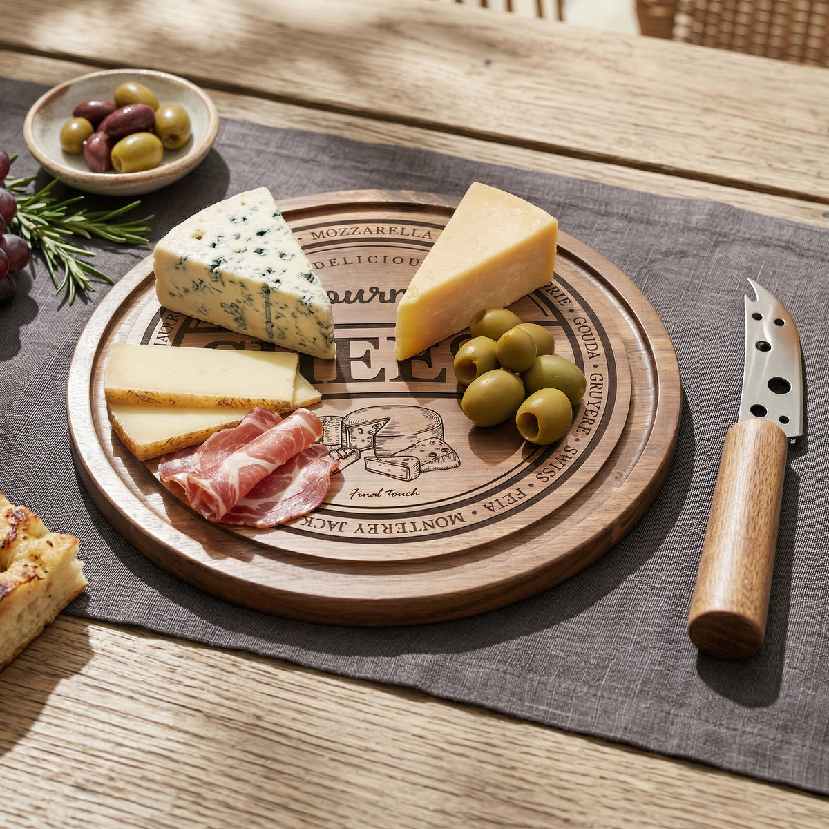 Wooden cheese board set with assorted cheeses, meats, and fruits on a wooden table.