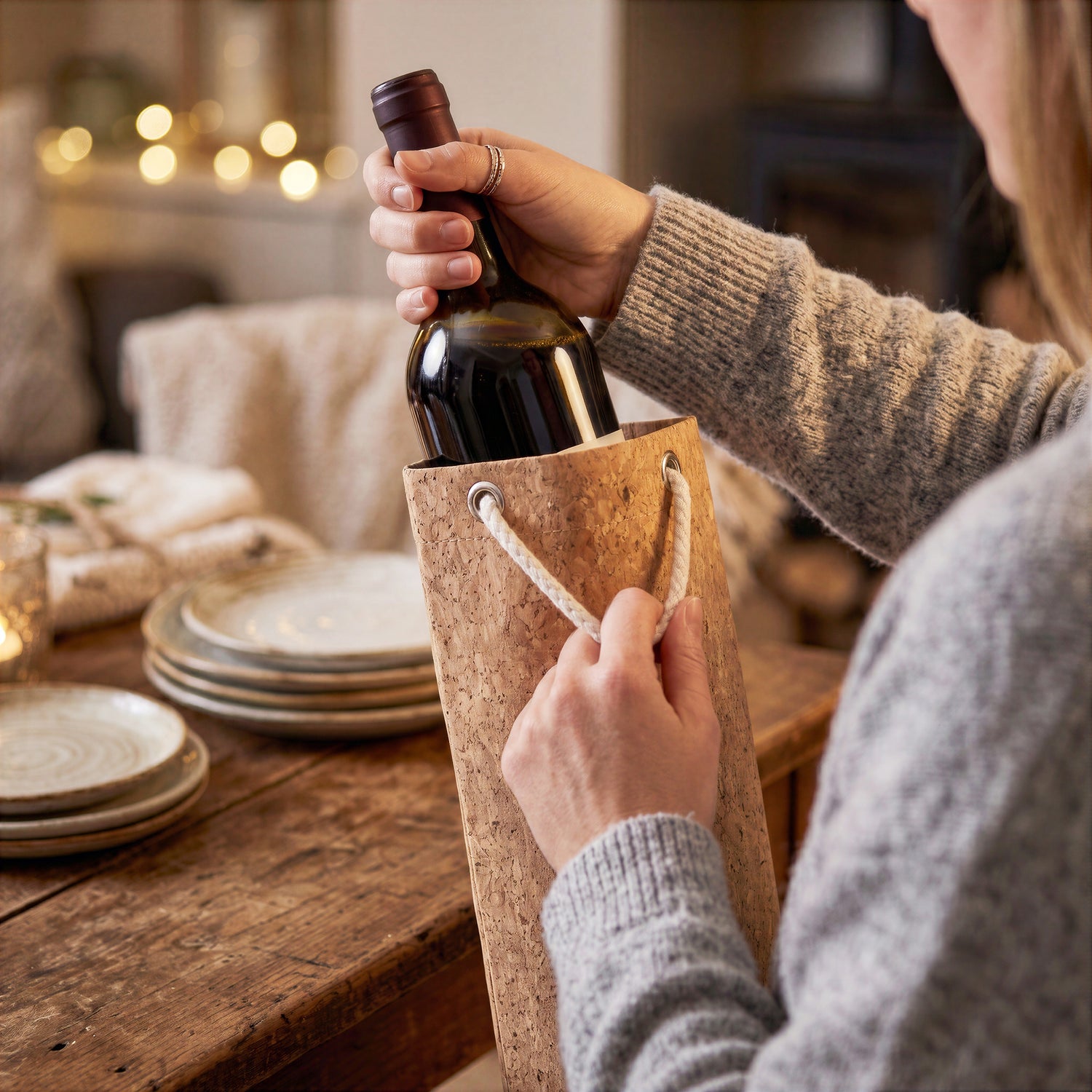 Person pulling a wine bottle out of a Final Touch cork wine gift bag on a cozy rustic dining table.