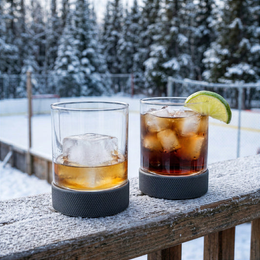 Final Touch lowball hockey glasses with black silicone puck bottoms holding whiskey and rum on a snowy winter deck.