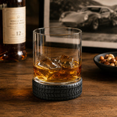 Tire base whiskey tumbler glass with whiskey and ice in a classic car inspired bar setting