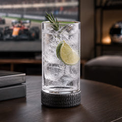 Automotive-inspired highball glass with silicone tire base holding a sparkling seltzer cocktail with lime and ice in a Formula 1 themed living room setting