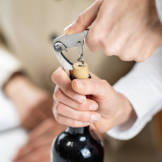 Stainless steel corkscrew with chrome-plated spiral, used to open a wine bottle.