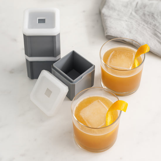 Stackable grey ice moulds with white lids, filled with orange drink and garnished with citrus peel.