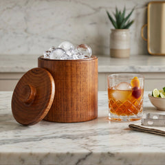 Final Touch Solid Wood Ice Bucket next to a crystal cocktail glass with a large ice sphere on a marble countertop.