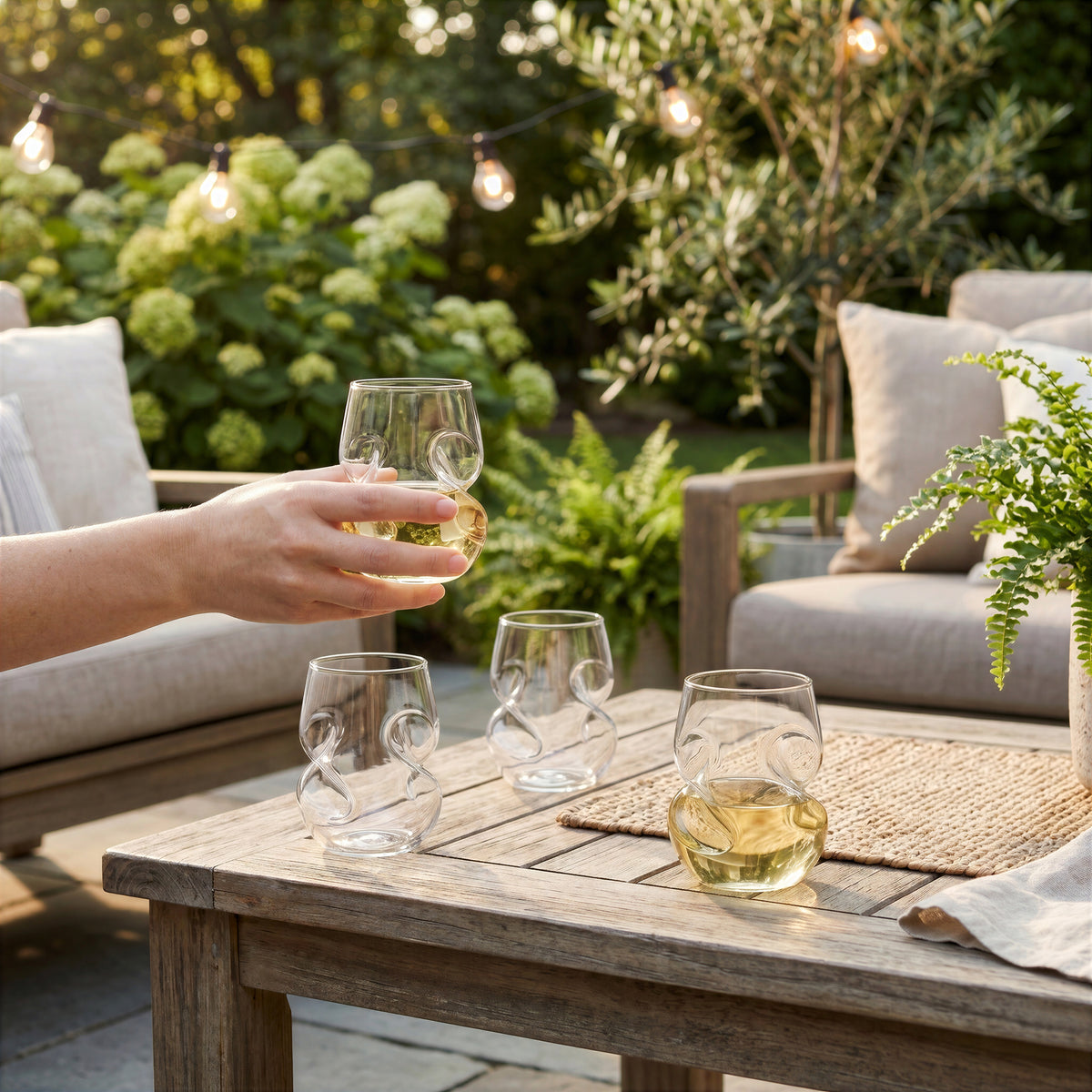 Final Touch Conundrum Stemless White Wine Glasses and bottle on a backyard patio table.
