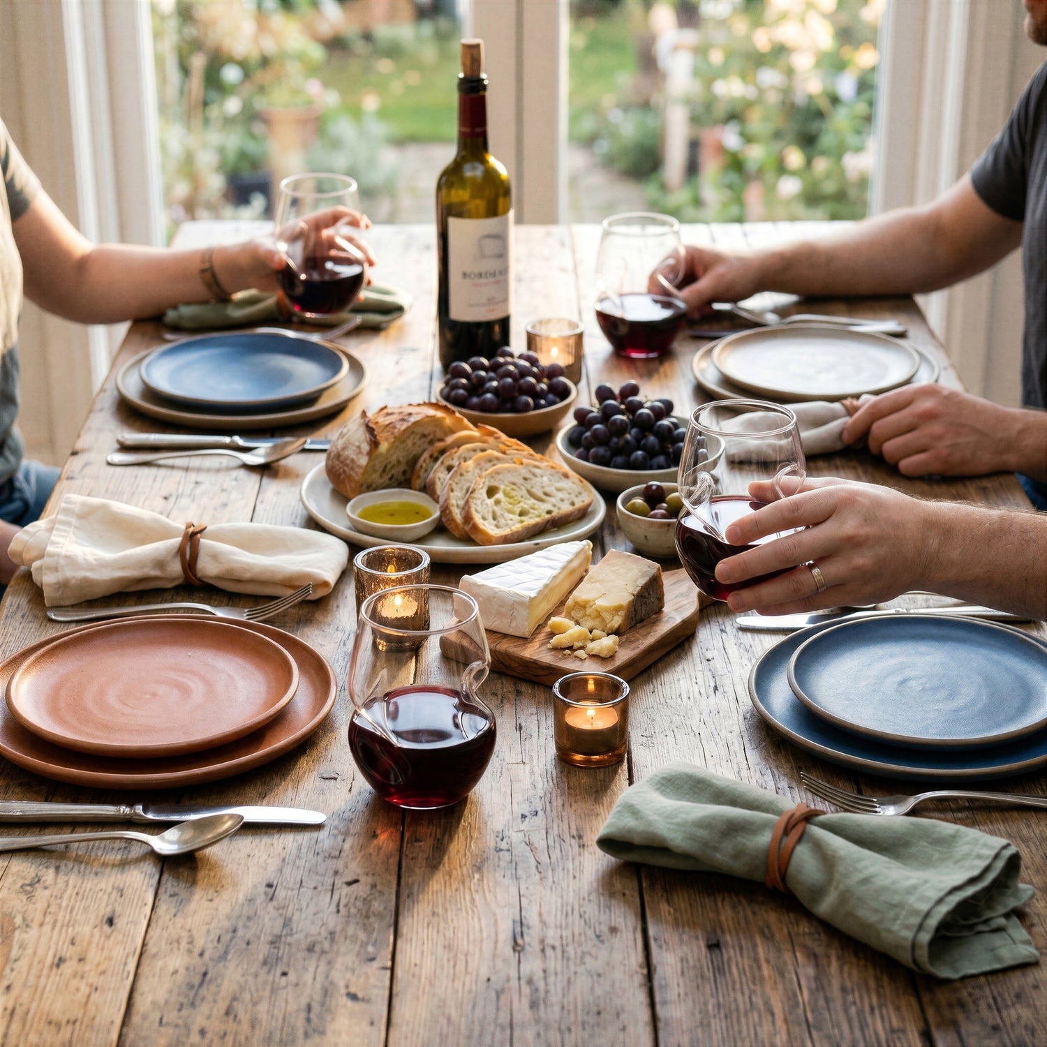 Friends enjoying a dinner party with red wine served in four Final Touch Conundrum Stemless Red Wine Glasses on with built-in finger grips, featuring a cozy Mediterranean-style spread.