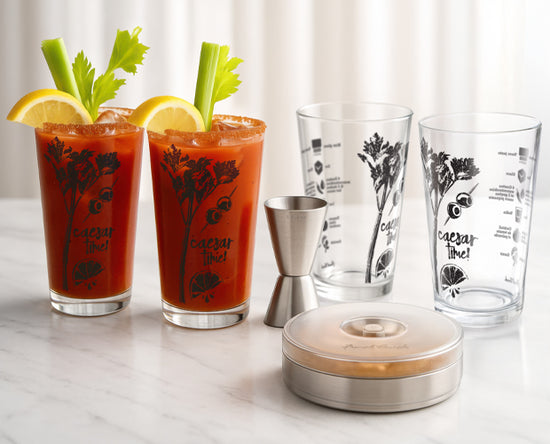 Two glasses of Caesar salad cocktail, garnished with celery and lemon slices, displayed on a marble countertop.