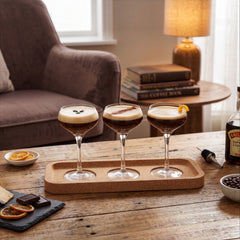 Final Touch Espresso Martini Flight Set with three cocktail coupe glasses served on a cork serving tray over a rustic wooden coffee table.