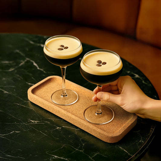 Espresso Martini drinks with a hand holding one on a cork tray flight.