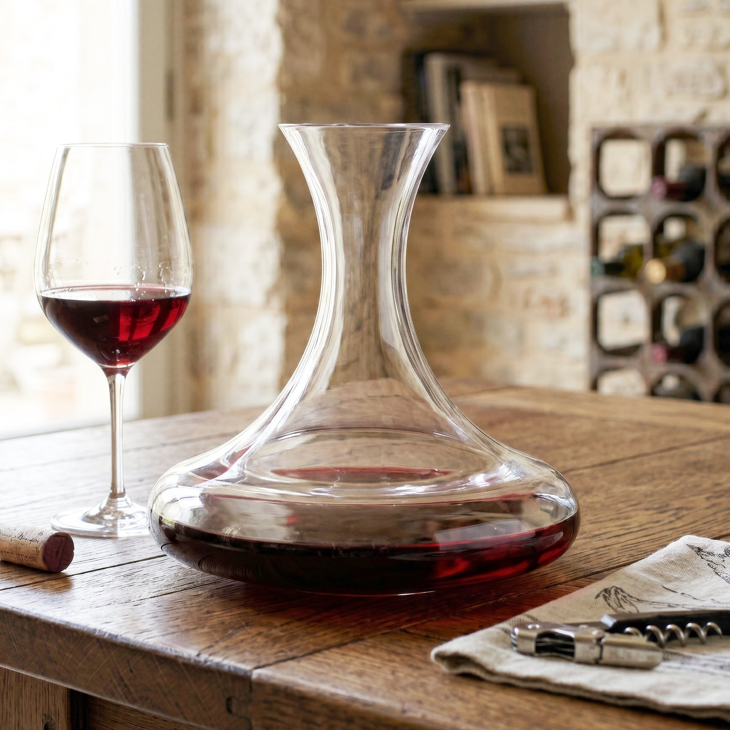 Luxury crystal red wine decanter by Final Touch, showing the wide-base aerating design in a warm, rustic home interior background.