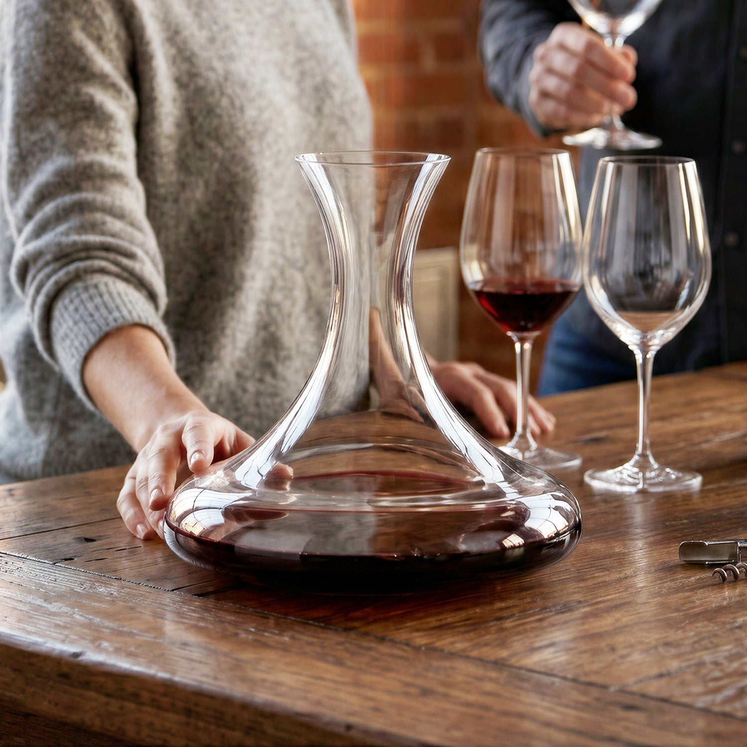 Final Touch Revolve revolving wine decanter with wide base on a rustic wooden table in a lifestyle kitchen setting with red wine glasses and bottles.