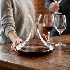 Final Touch Revolve revolving wine decanter with wide base on a rustic wooden table in a lifestyle kitchen setting with red wine glasses and bottles.