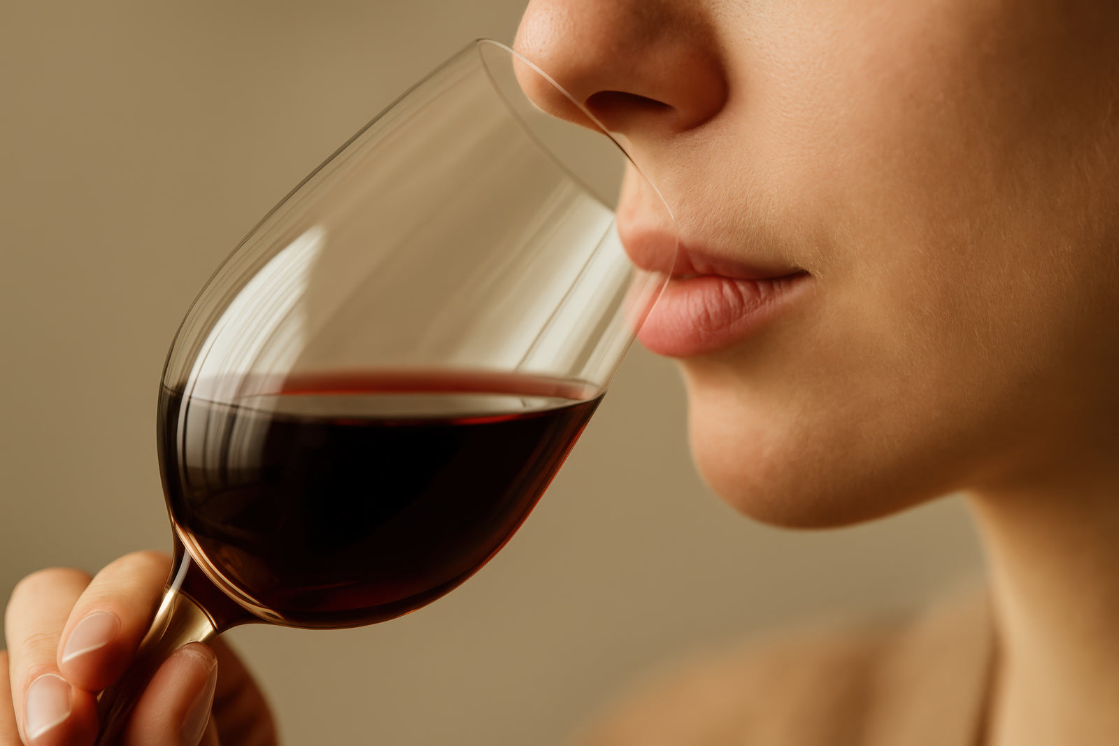 Close-up of a person holding a Final Touch Wine Tasting Glass with red wine, shown from the side against a warm beige background.
