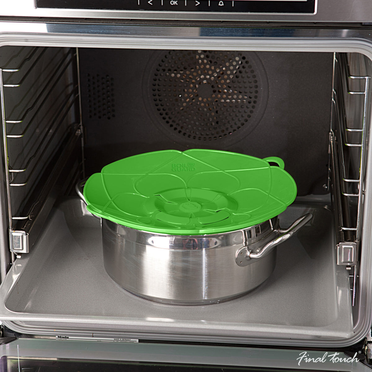 Green lid covers a stainless steel saucepan inside an oven.