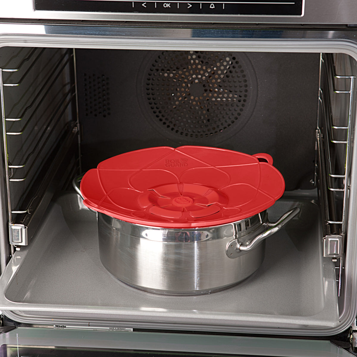 Red lid covers stainless steel saucepan inside oven.
