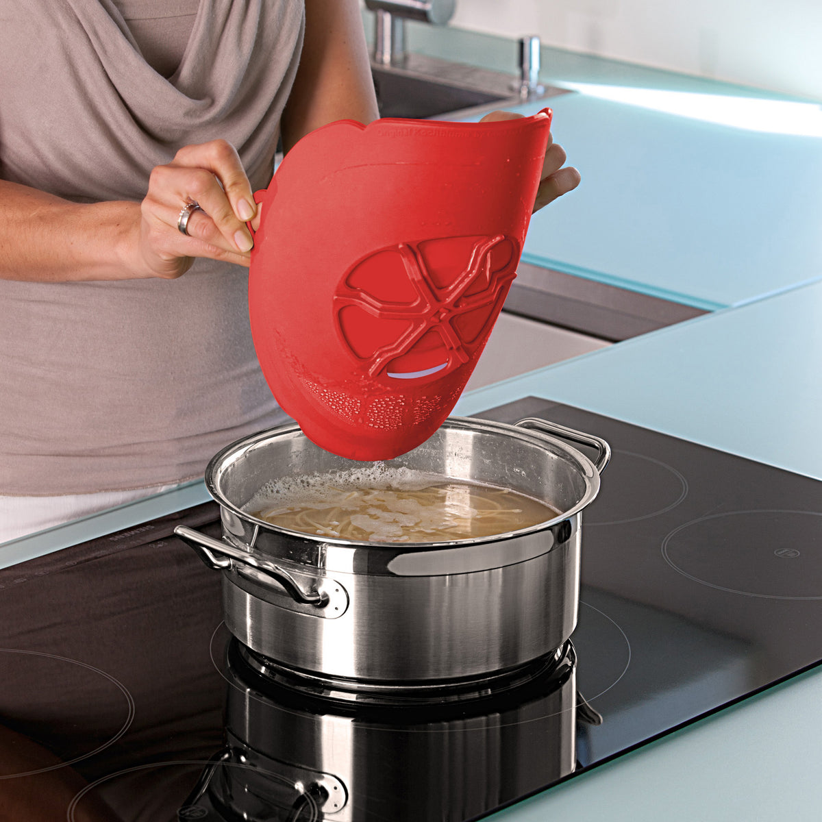 A red silicone boil guard rests on a stainless steel pot, ready for use.