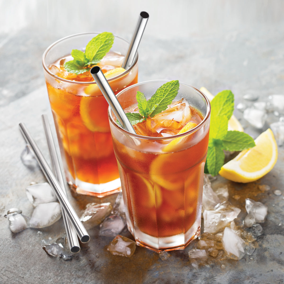Two stainless steel straws in a glass of iced tea with mint and lemon.